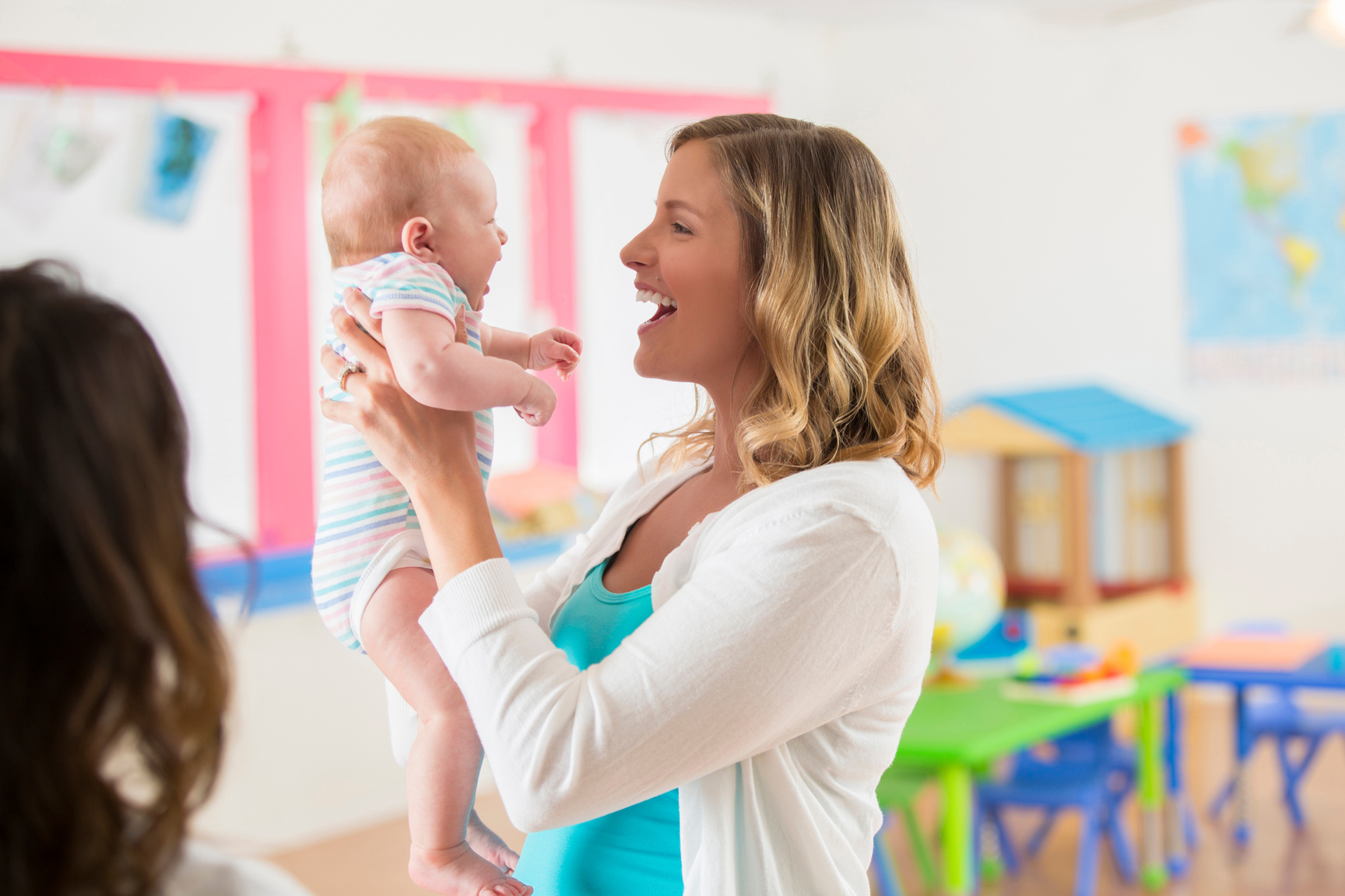Laughing mother holding her sweet infant baby girl in daycare